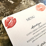 The Punctilious Mr. P's Place Card Co. 'Kisses' custom Mayfair size menu of lips on a black marble tabletop