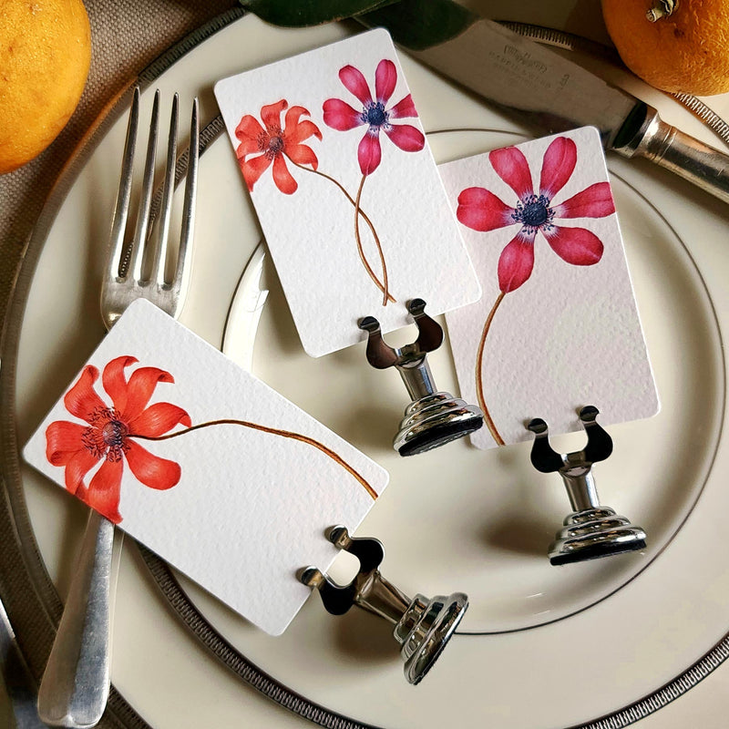 showing all 3 anemones of The Punctilious mr. P's Pace Card Co. "anemones" custom place card on a silver place card holder with magnolia leaves and lemons in the background against a chinoiserie screen