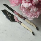 video of Two Laguiole cake knives with beige handles on a marble surface with pink flowers.