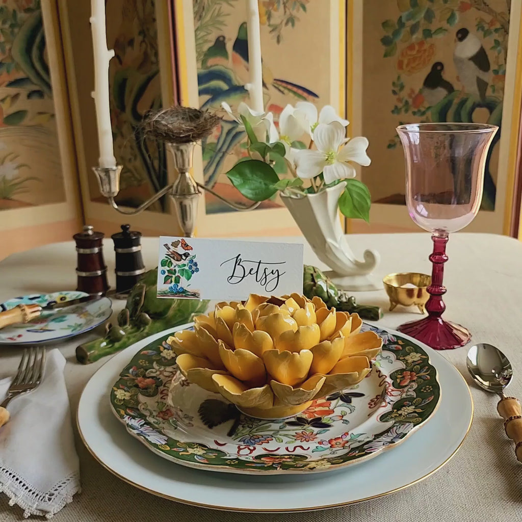 Decorative table setting with a 'Betsy' name place card and yellow ceramic blossom centerpiece.