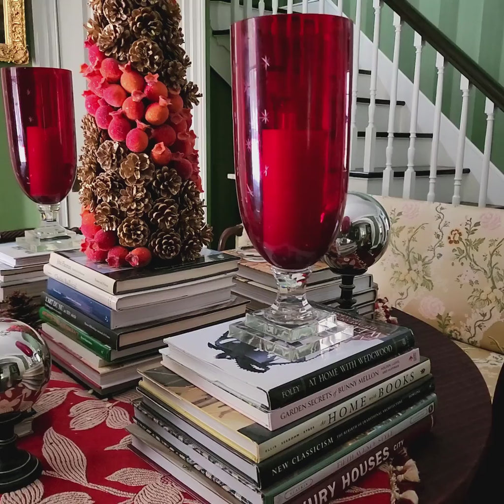 video of Decorative red hurricane candle holders on a stack of books with a staircase and green walls in the background