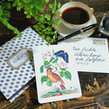 video of Illustrated note Card with a bird and butterfly design on a chinoiserie table with a montblanc teacup and pen.
