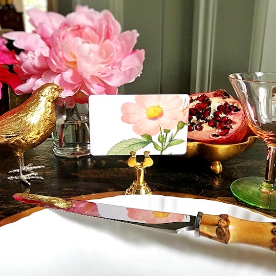 The Punctilious mr. P's Pace Card Co. "Garden Roses" custom place card on a gold place card holder with flowers and a pomegranate in the background