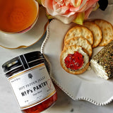 A jar of the Punctilious Mr. P's hot pepper jelly on a marble tabletop with trader joe's 'cracker assortment' and creamy herb chevre cheese