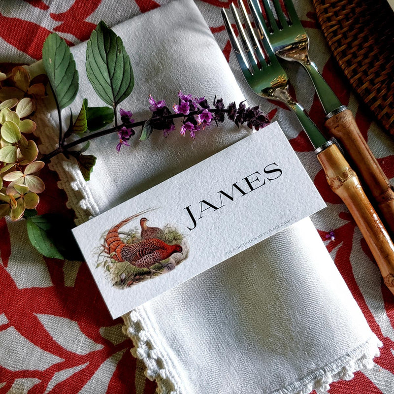 The Punctilious Mr. P's Place Card Co. 'Fiery Pheasants' custom laydown place card on top of linen napkin with bamboo cutlery and a red color blocked tablecloth