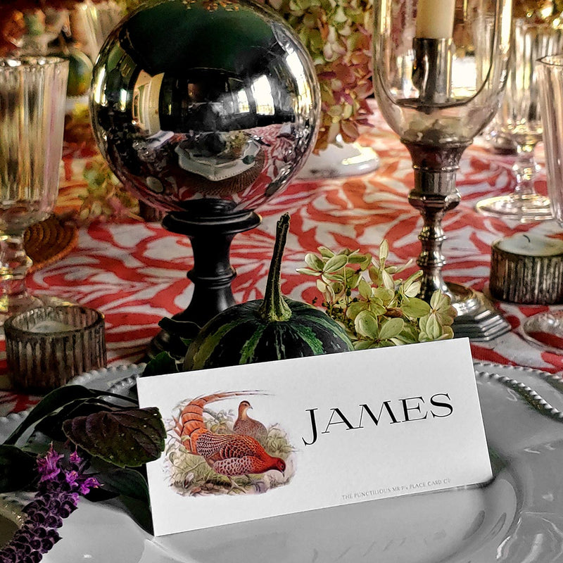 The Punctilious Mr. P's Place Card Co. 'Fiery Pheasants' custom laydown place card on top of linen napkin with bamboo cutlery and a red color blocked tablecloth