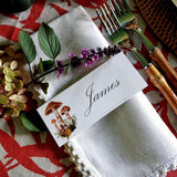 The Punctilious Mr. P's Place Card Co. 'Red Bands Mushroom' laydown custom place card on top of linen napkin with bamboo cutlery and a red color blocked tablecloth