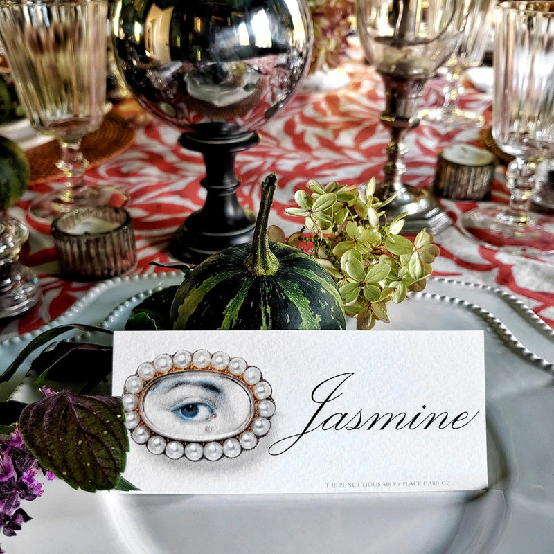 The Punctilious Mr. P's Place Card Co. 'Lover's Eye' custom laydown place card on top of linen napkin with bamboo cutlery and a red color blocked tablecloth