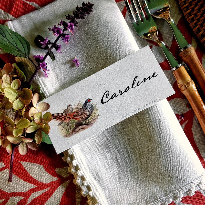 The Punctilious Mr. P's Place Card Co. 'Pheasantry' custom laydown place card on top of linen napkin with bamboo cutlery and a red color blocked tablecloth