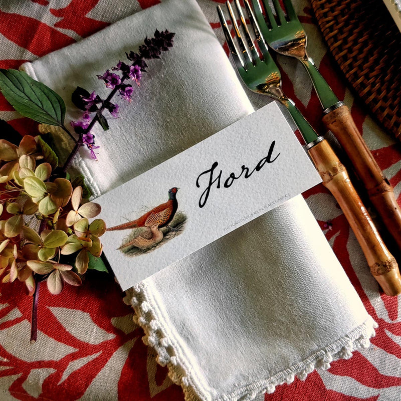 The Punctilious Mr. P's Place Card Co. 'Pheasantry' custom laydown place card on top of linen napkin with bamboo cutlery and a red color blocked tablecloth