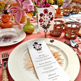 Marian McEvoy's bistro size pressed poppy Custom  menu sits atop tablescape of Christopher Spitzmiller's dahlia dinner plates, wicker cutlery and red creel & gow tablecloth with beautiful bud vases and flowers and coordinating place cards