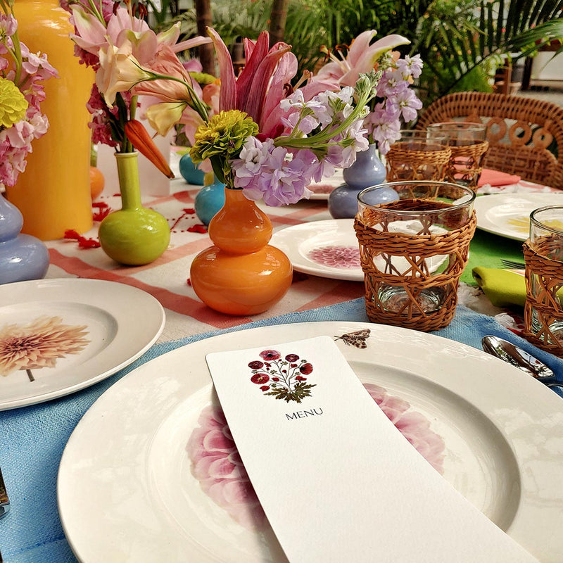 Marian McEvoy's blank bistro size pressed poppy custom menu sits atop tablescape of Christopher Spitzmiller's dahlia dinner plates, wicker cutlery and red creel & gow tablecloth with beautiful bud vases and flowers