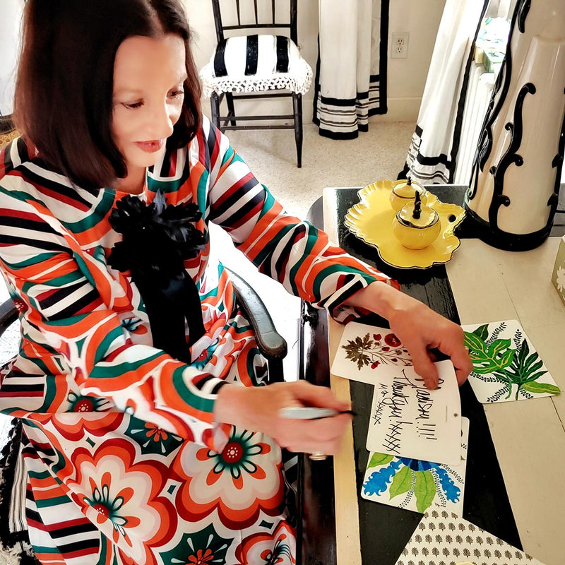 Marian McEvoy writing note cards at her desk, wearing a beautiful and colorful floral dress