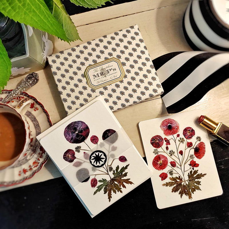 Marian McEvoy x The Punctilious Mr. P's Place Card Co collab with pressed poppies botanical illustrated custom note cards on a table with ribbon, cup of coffee and a tube of red lipstick