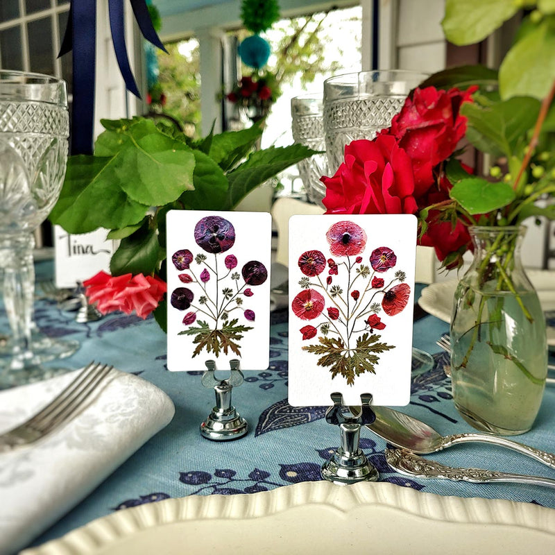 Marian McEvoy x The Punctilious Mr. P's Place Card Co collab with red and purple pressed poppies botanical illustrated custom place cards on a table with silverware, beautiful roses and fine cut crystal