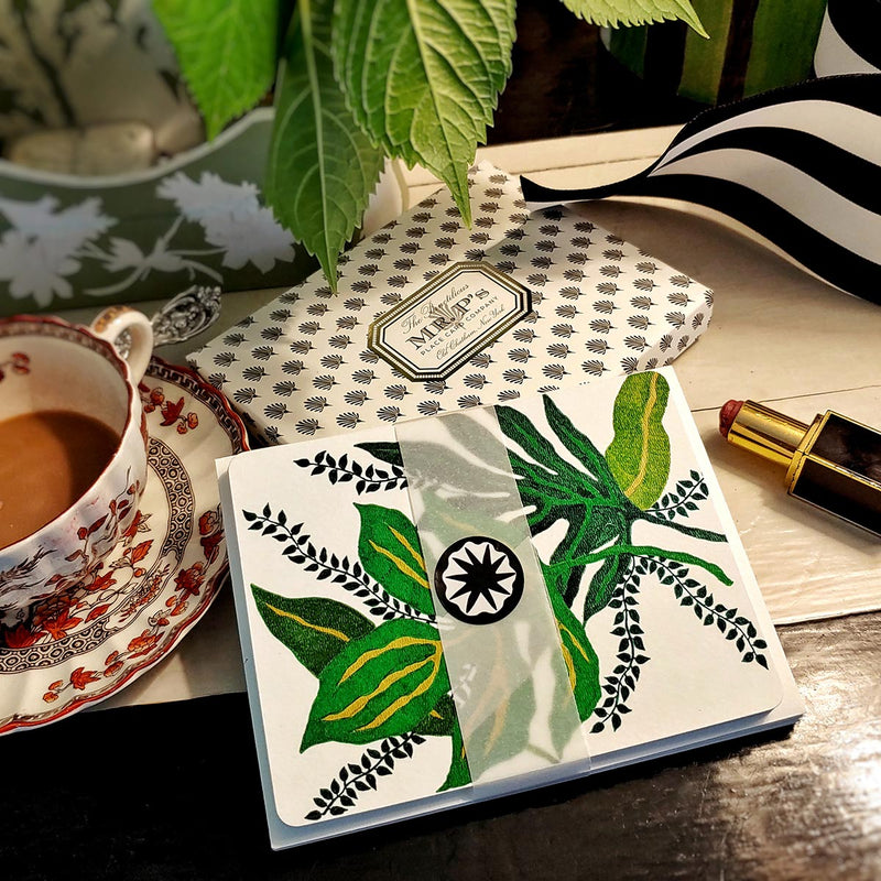 Marian McEvoy x The Punctilious Mr. P's Place Card Co collab with "tropicalia verde' botanical illustrated custom note cards on a table with ribbon, cup of coffee and a tube of red lipstick