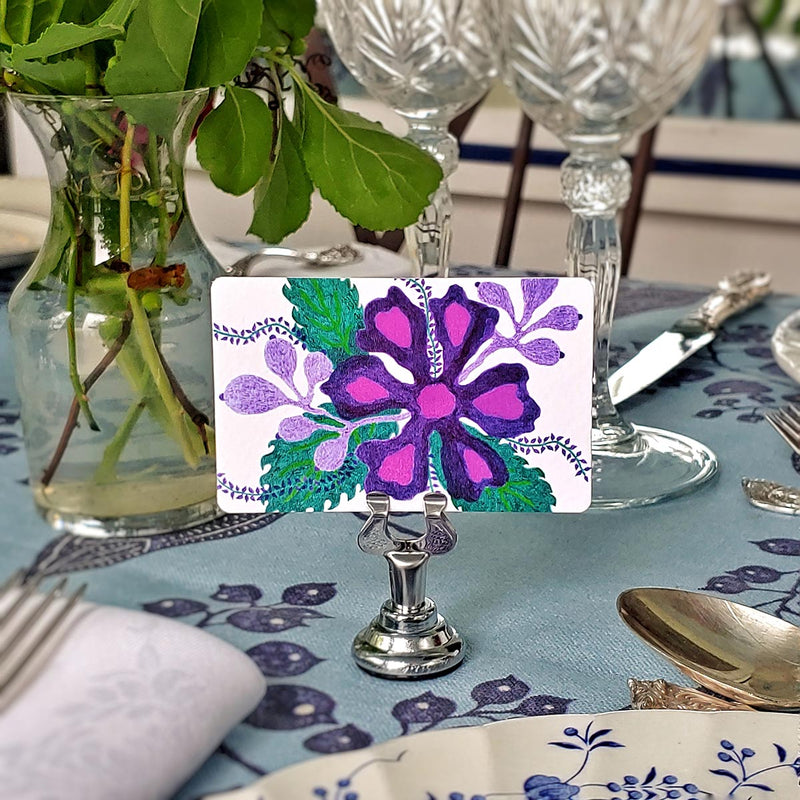 Marian McEvoy x The Punctilious Mr. P's Place Card Co collab with tropical purple floral Custom  illustrated place cards on a table with silverware and beautiful cut crystal