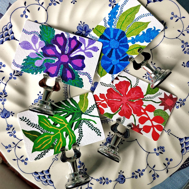 Marian McEvoy x The Punctilious Mr. P's Place Card Co collab with all four tropical floral Custom  illustrated place card colorways in red, blue, green and purple on blue and white pattern dinner plate.