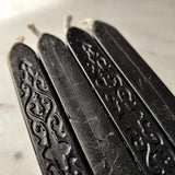 detail of The Punctilious Mr. P's place card co. embossed flourish design on the side of 4 black wick wax sticks used for stamp seal