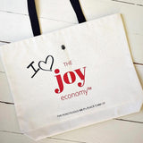The Punctilious Mr. P's Everyday natural colored canvas tote bag with "I heart" written next to the joy economy logo on back with black web handle